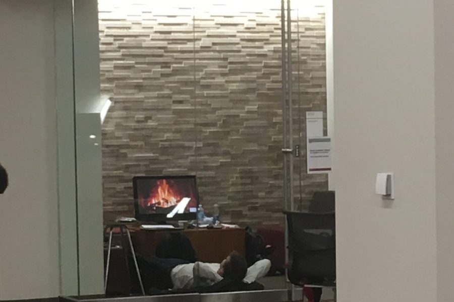 student lying on the ground watching a screen with fireplace on it in group study room